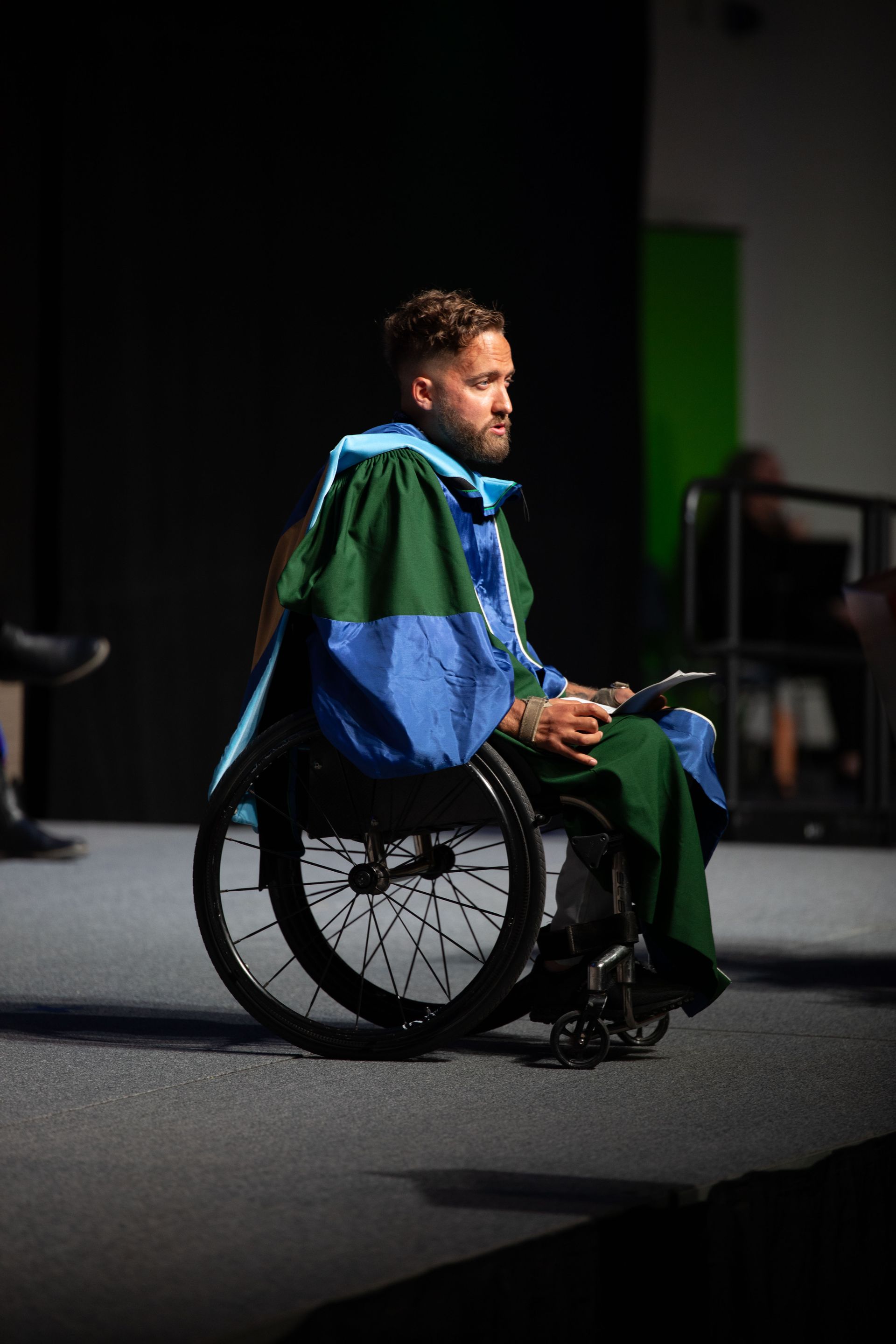 A man in a gown is sitting in a wheelchair on a stage.