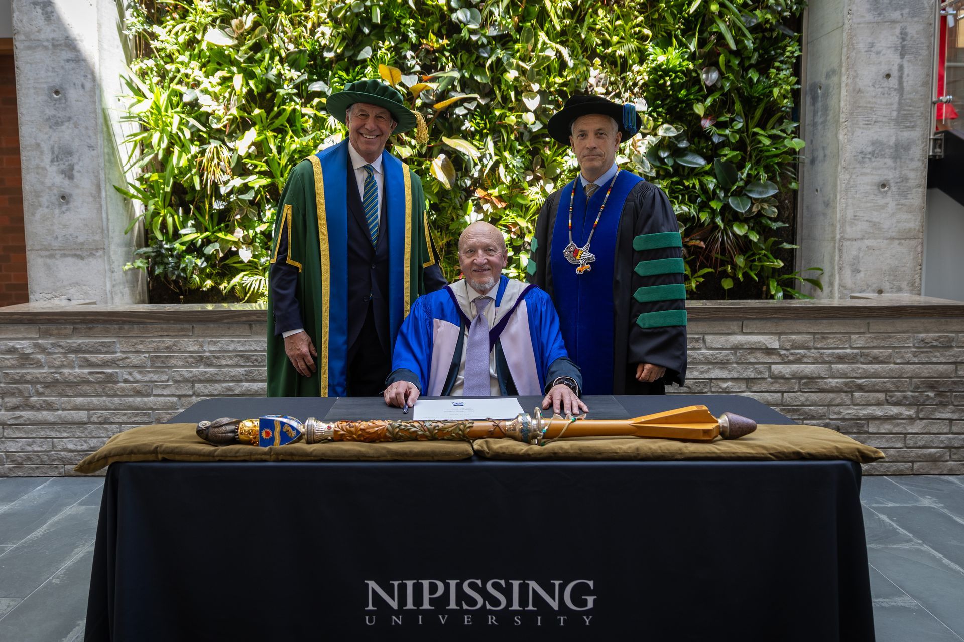 Three people pose behind a signed table at Nipissing University