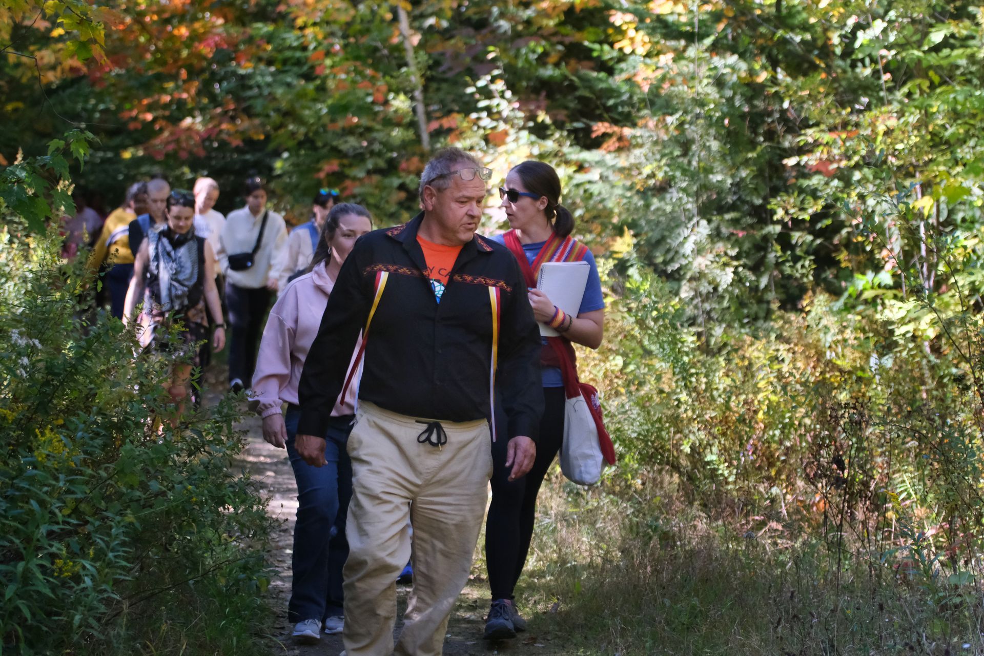 Group of people walking on a wooded path in autumn; trees with fall colors.