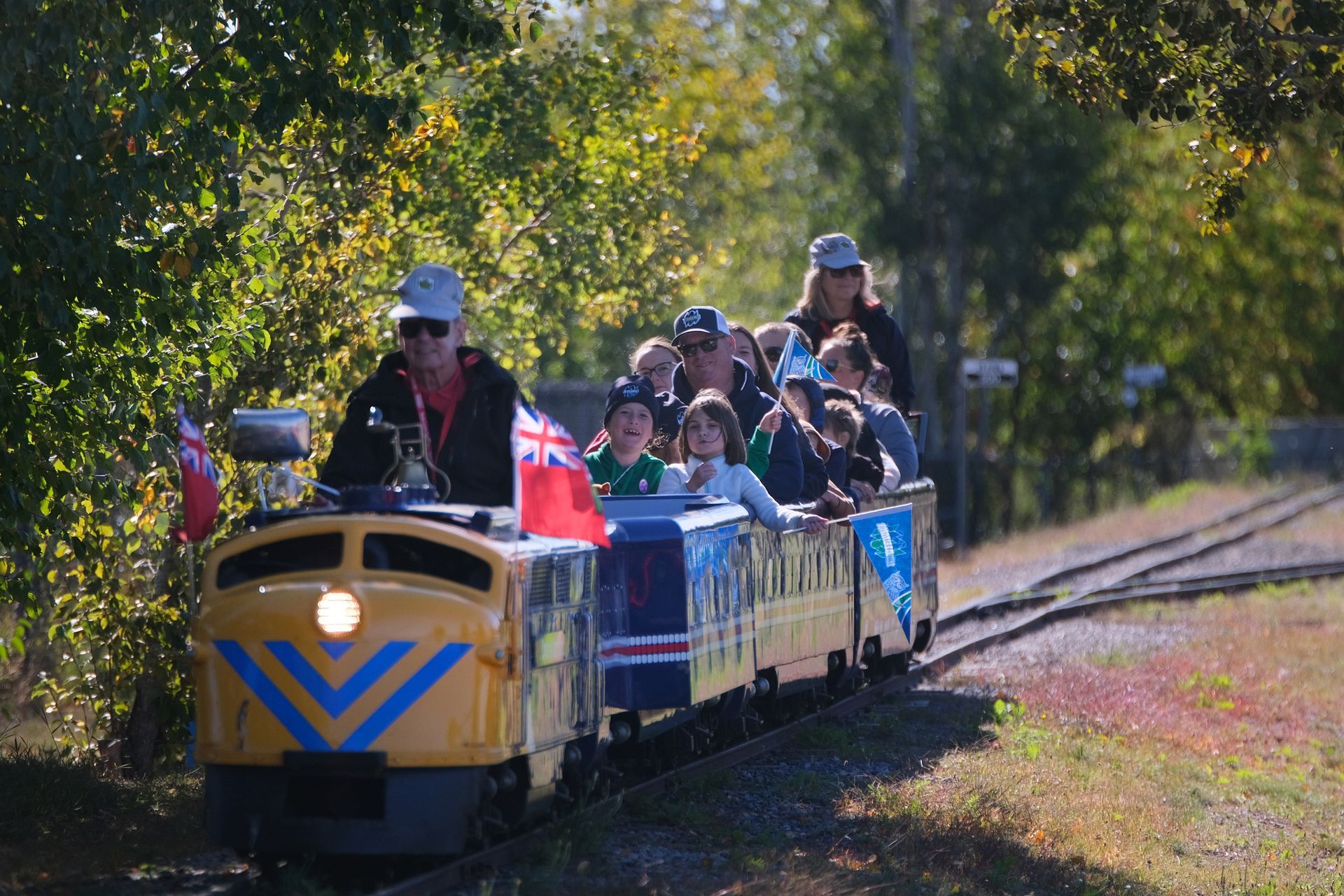Yellow train with children on tracks, in a green, sunny setting.