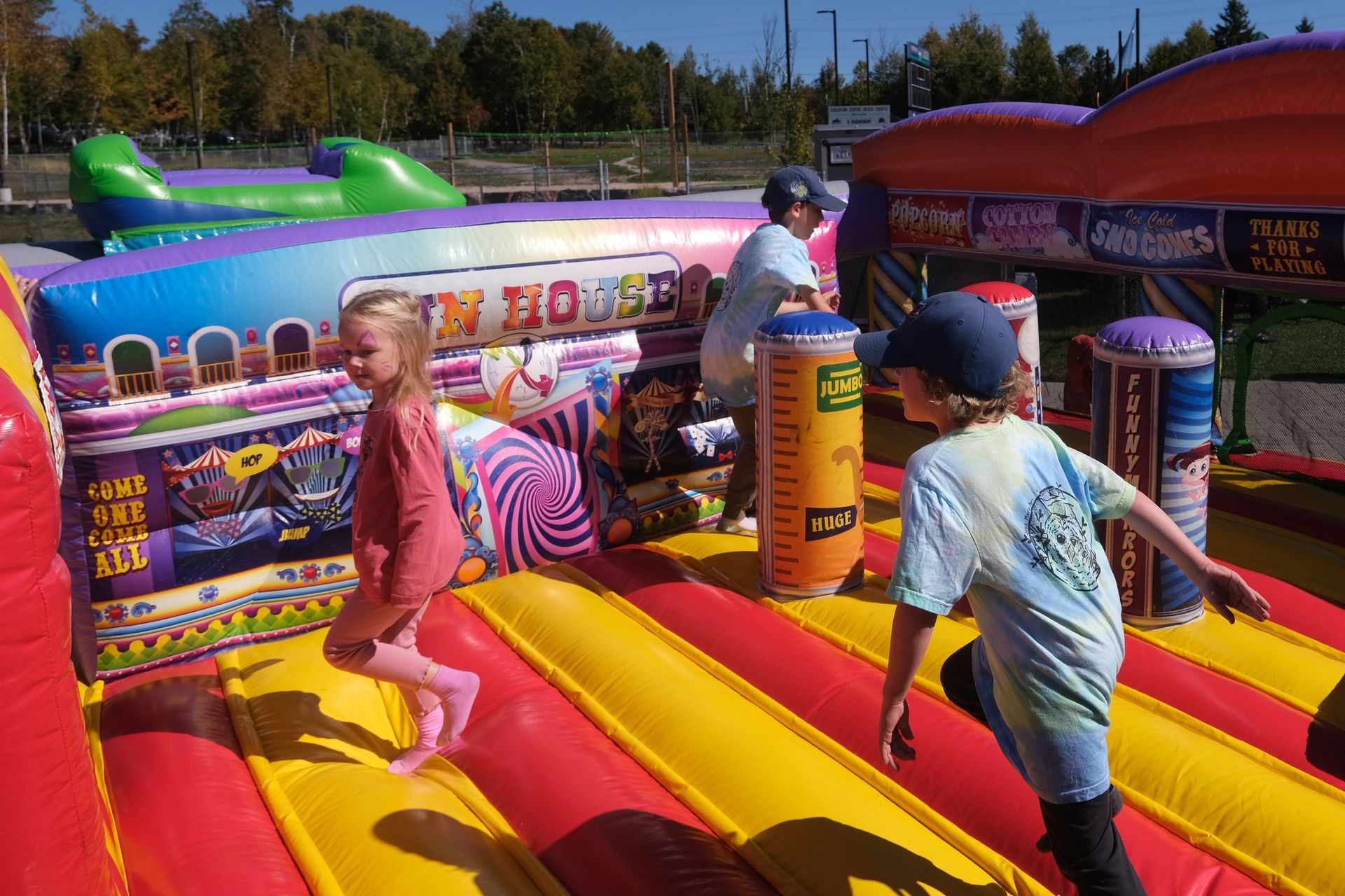 Children playing on a colorful inflatable bounce house outdoors on a sunny day.