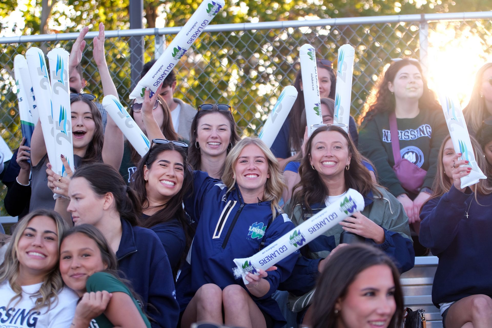 Fans cheering at a sports game. Women smiling, raising arms, in outdoor stadium.