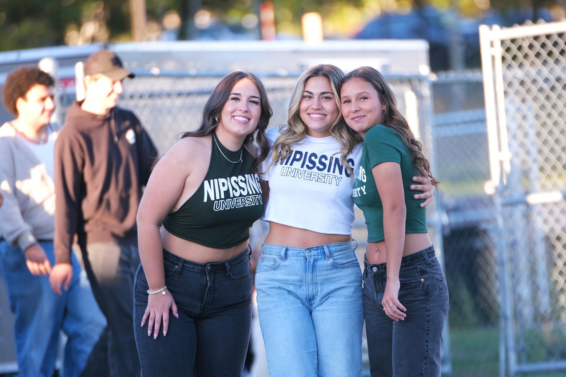 Three young women in crop tops pose outdoors.