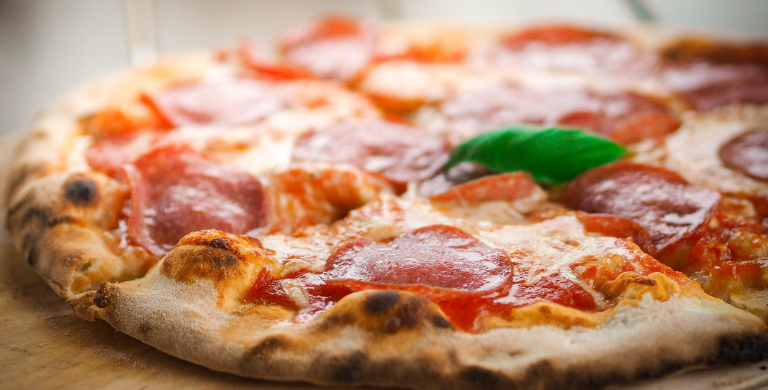 A close up of a pepperoni pizza on a wooden cutting board.