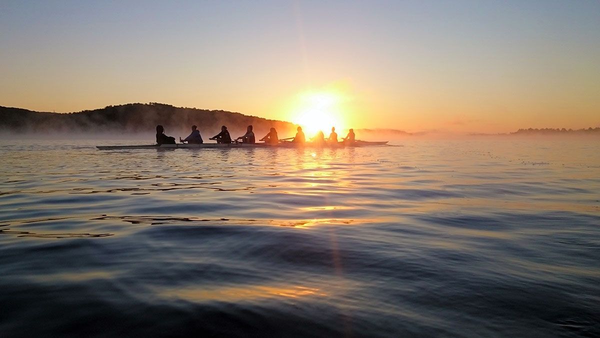 A group of people are rowing a boat in the water at sunset