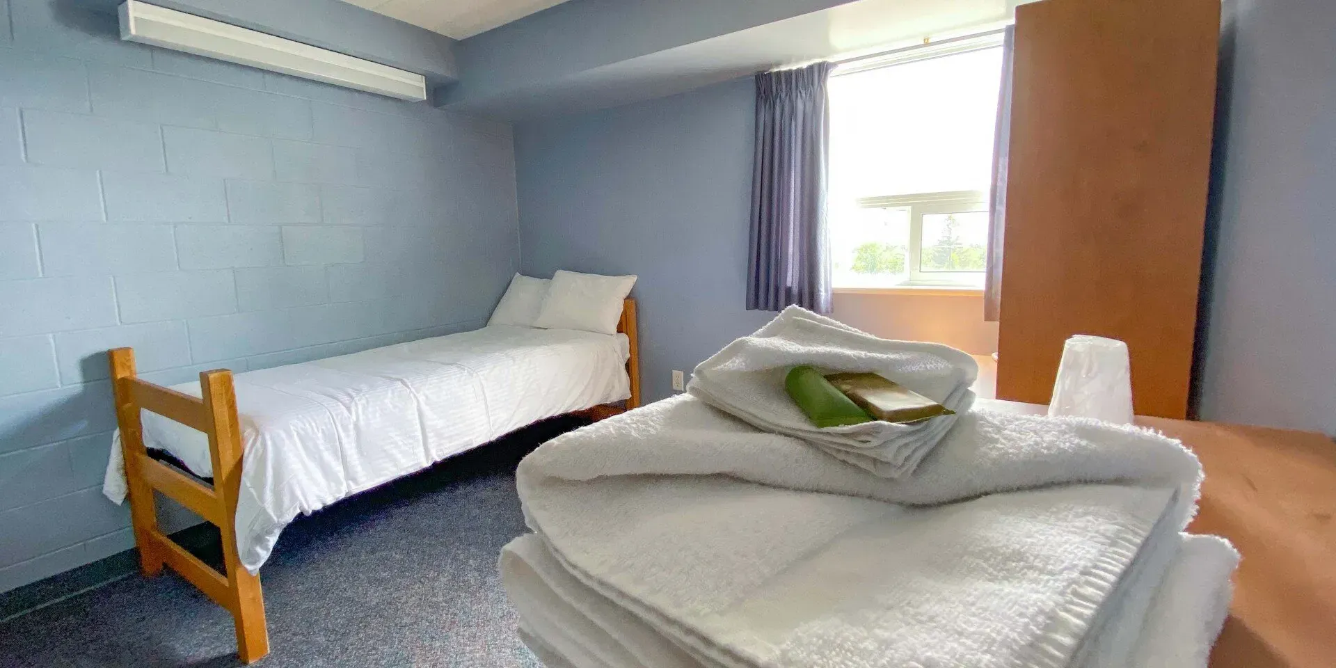 A bedroom with a single bed and a stack of towels.