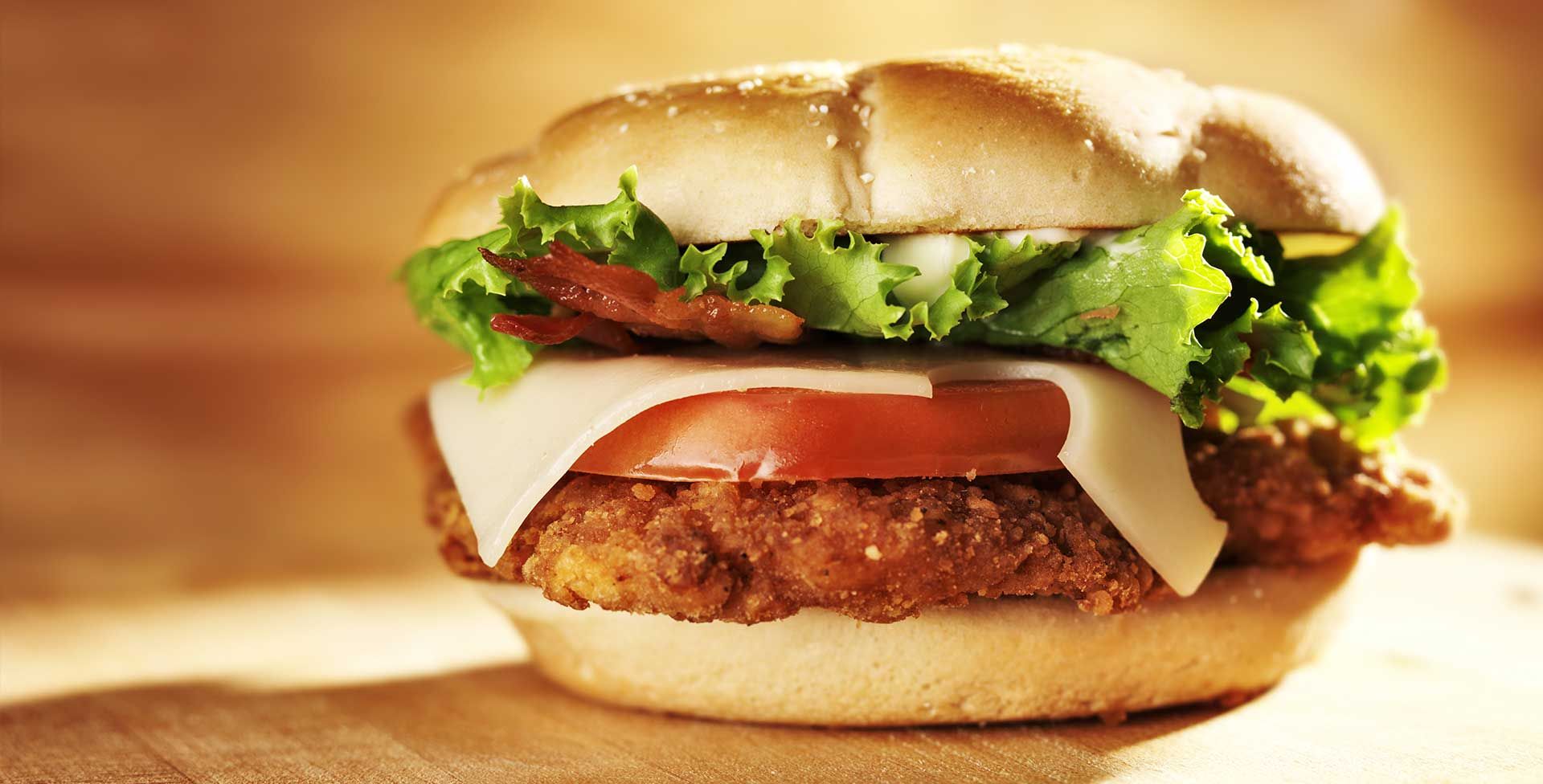 A chicken sandwich with lettuce, tomato and cheese on a bun