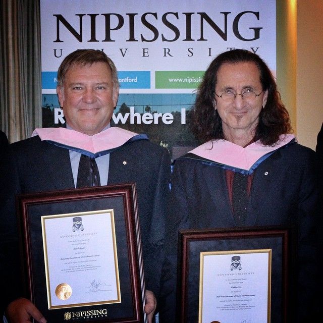 Two men in academic gowns holding framed diplomas at Nipissing University.