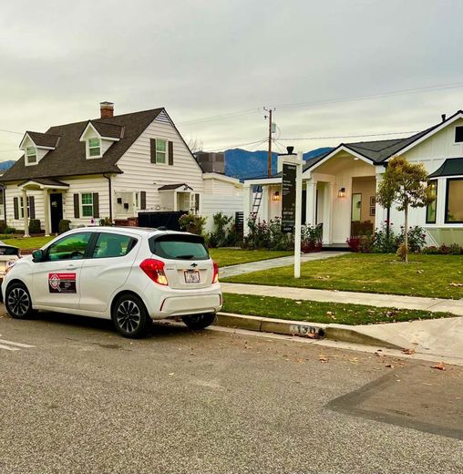A white car is parked on the side of the road in front of a row of houses.