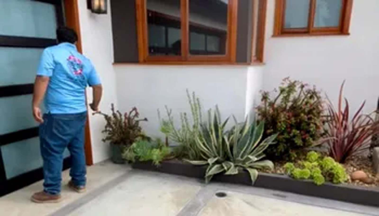 A man in a blue shirt is standing in front of a house.