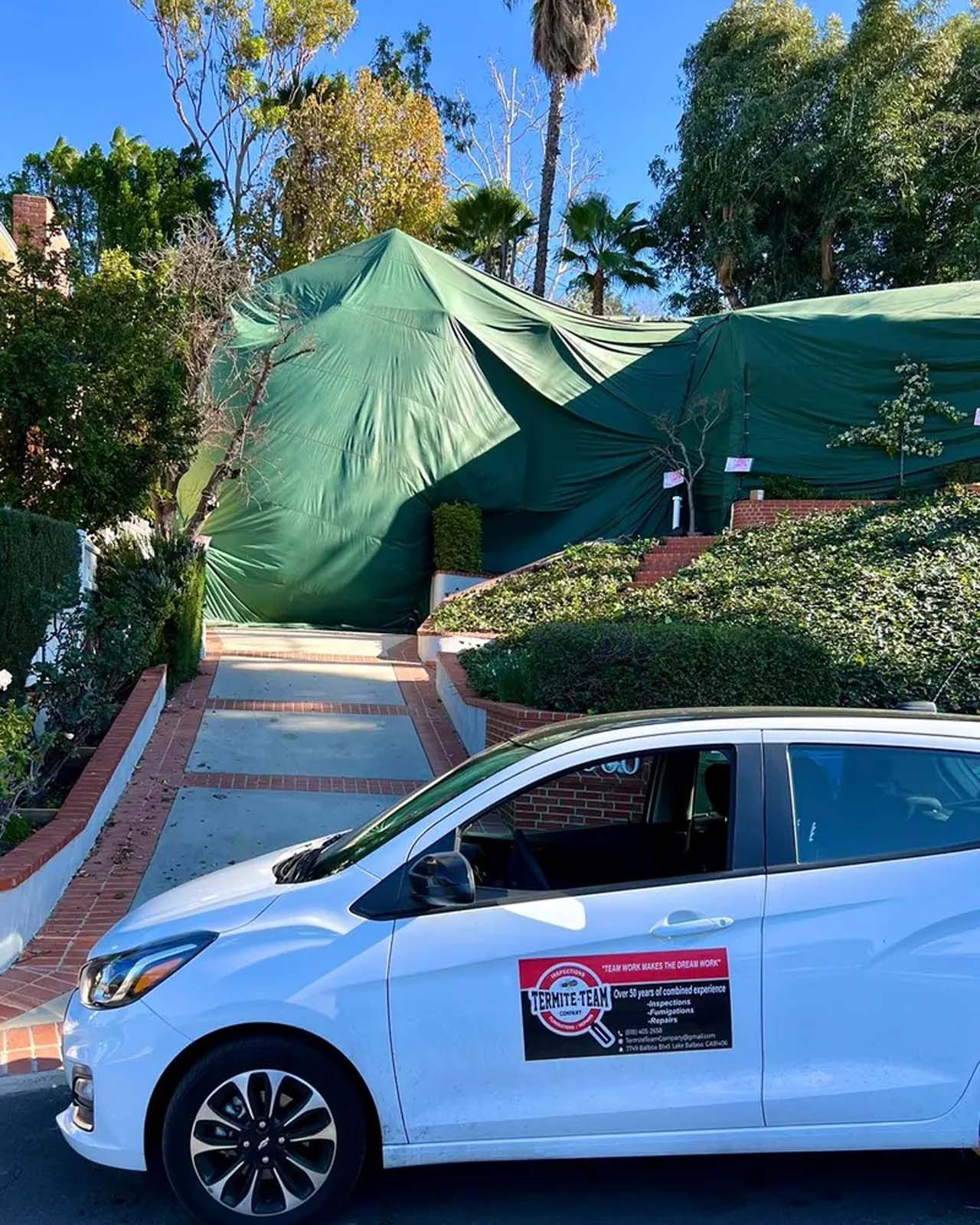 A white car is parked in front of a green tent.