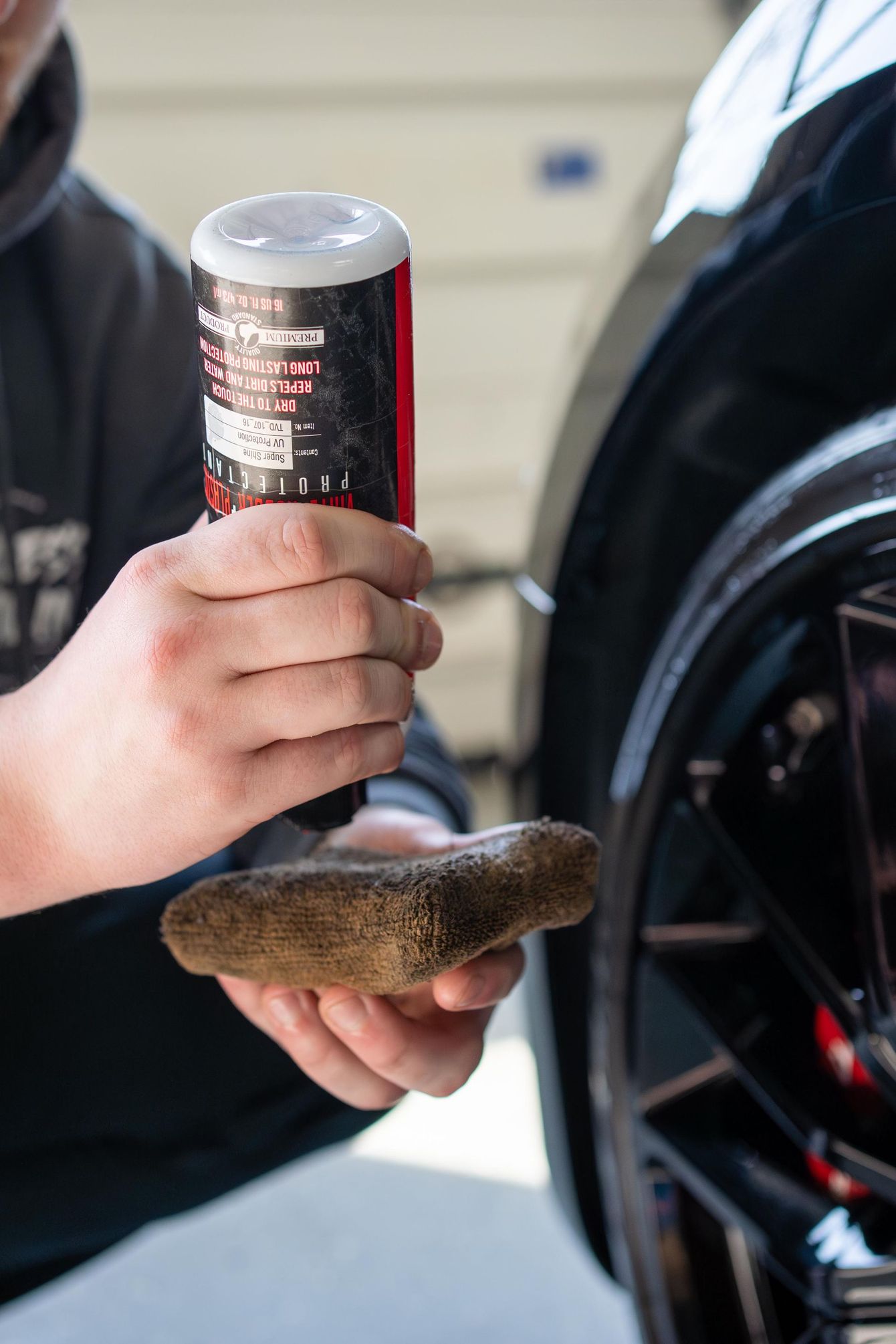 Person applying a car care product to a sponge near a car's wheel.