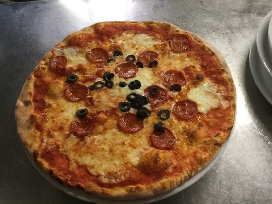 Una pizza con peperoni e olive è su un piatto su un tavolo.