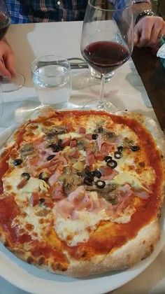 Una pizza è appoggiata su un piatto bianco su un tavolo accanto a un bicchiere di vino.