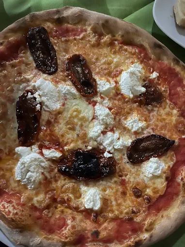Una pizza con formaggio, pomodori e pomodori secchi su un tavolo.