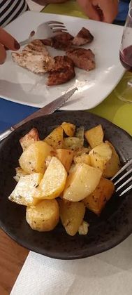 Un piatto di patate con una forchetta su un tavolo accanto a un piatto di carne.