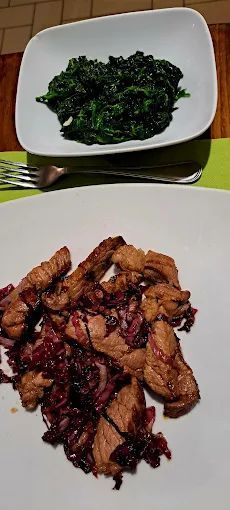 Un piatto bianco con sopra carne e verdure accanto a una ciotola di spinaci.