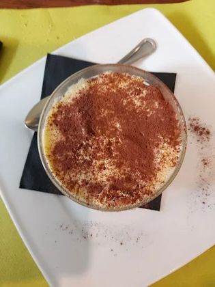 Una ciotola di tiramisù con un cucchiaio su un piatto bianco