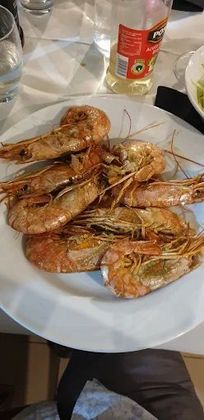 Un piatto di gamberi è appoggiato su un tavolo accanto a una bottiglia di soda.