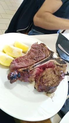 Un piatto bianco sormontato da un pezzo di carne e fette di limone.