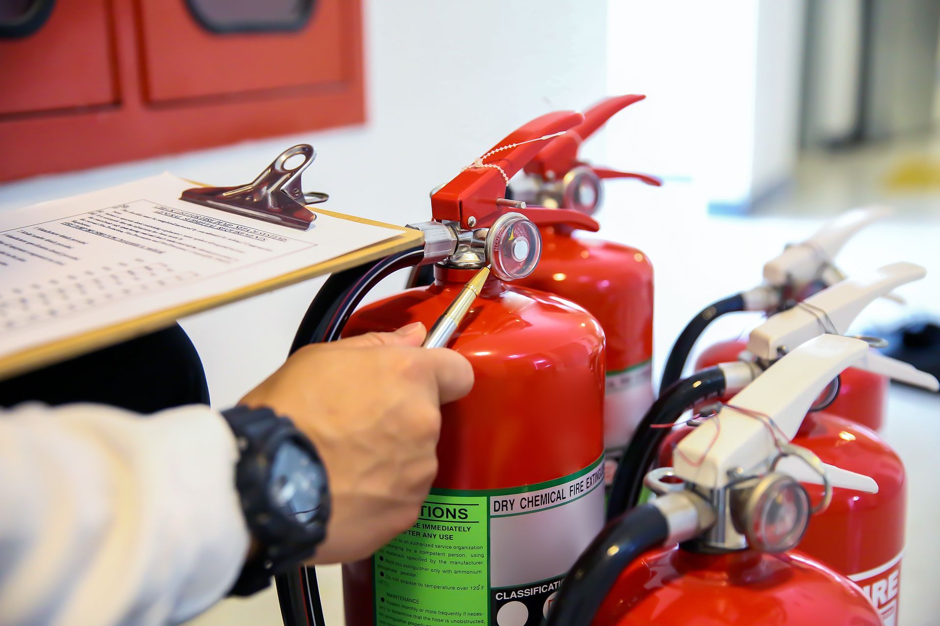Technician inspecting red fire extinguishers with a clipboard. Technician inspecting red fire extinguishers with a clipboard.