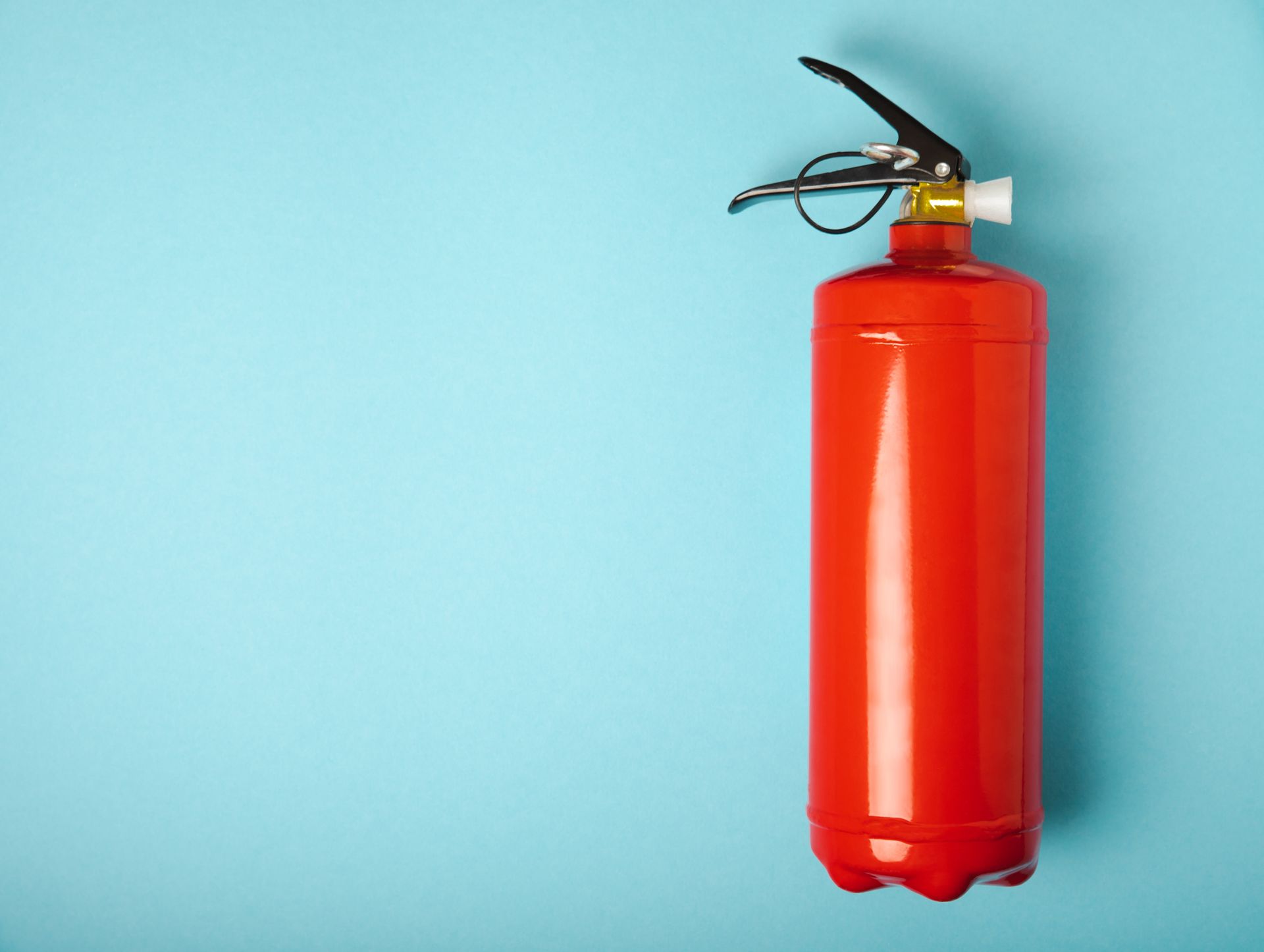 Red fire extinguisher securely mounted on a light blue wall.