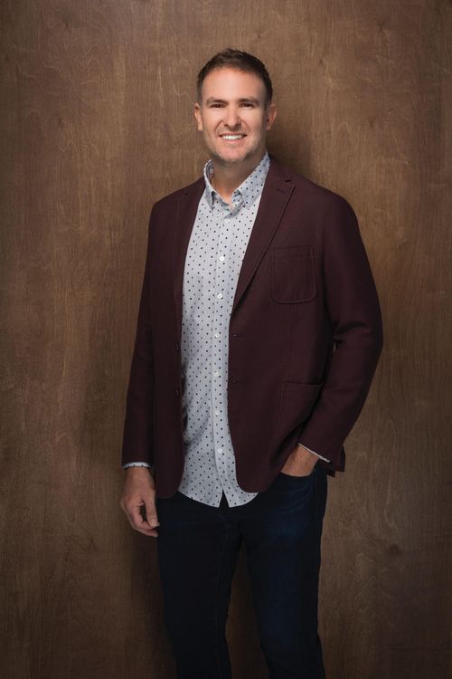 A man in a black scrub top is standing in front of a white wall.