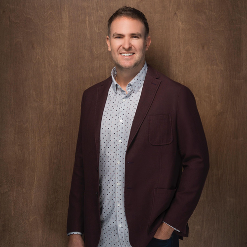 A man in a black scrub top is standing in front of a white wall.