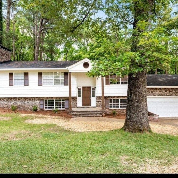 A white house with a tree in front of it surrounded by trees.