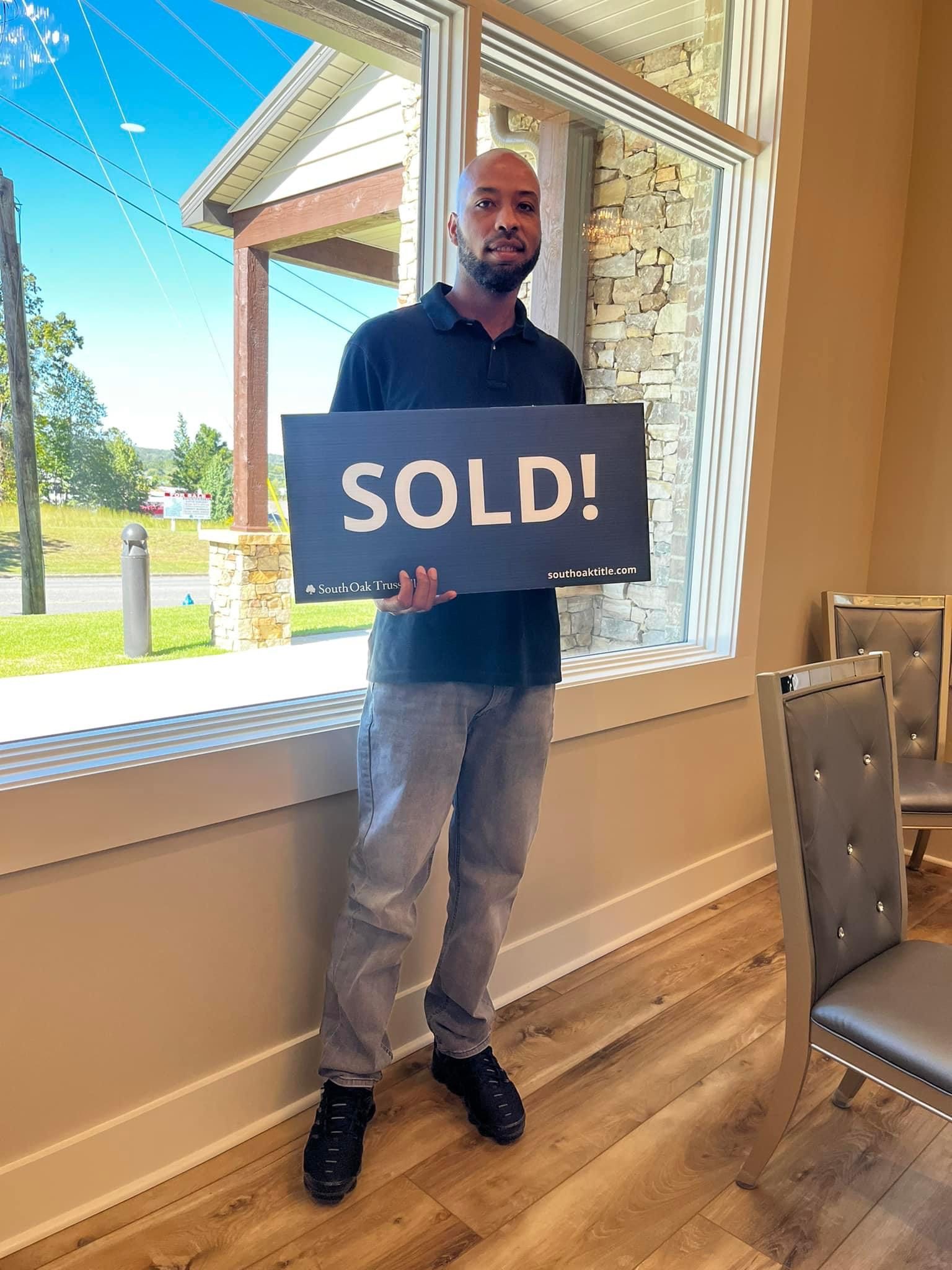 A man is holding a sold sign in front of a window.
