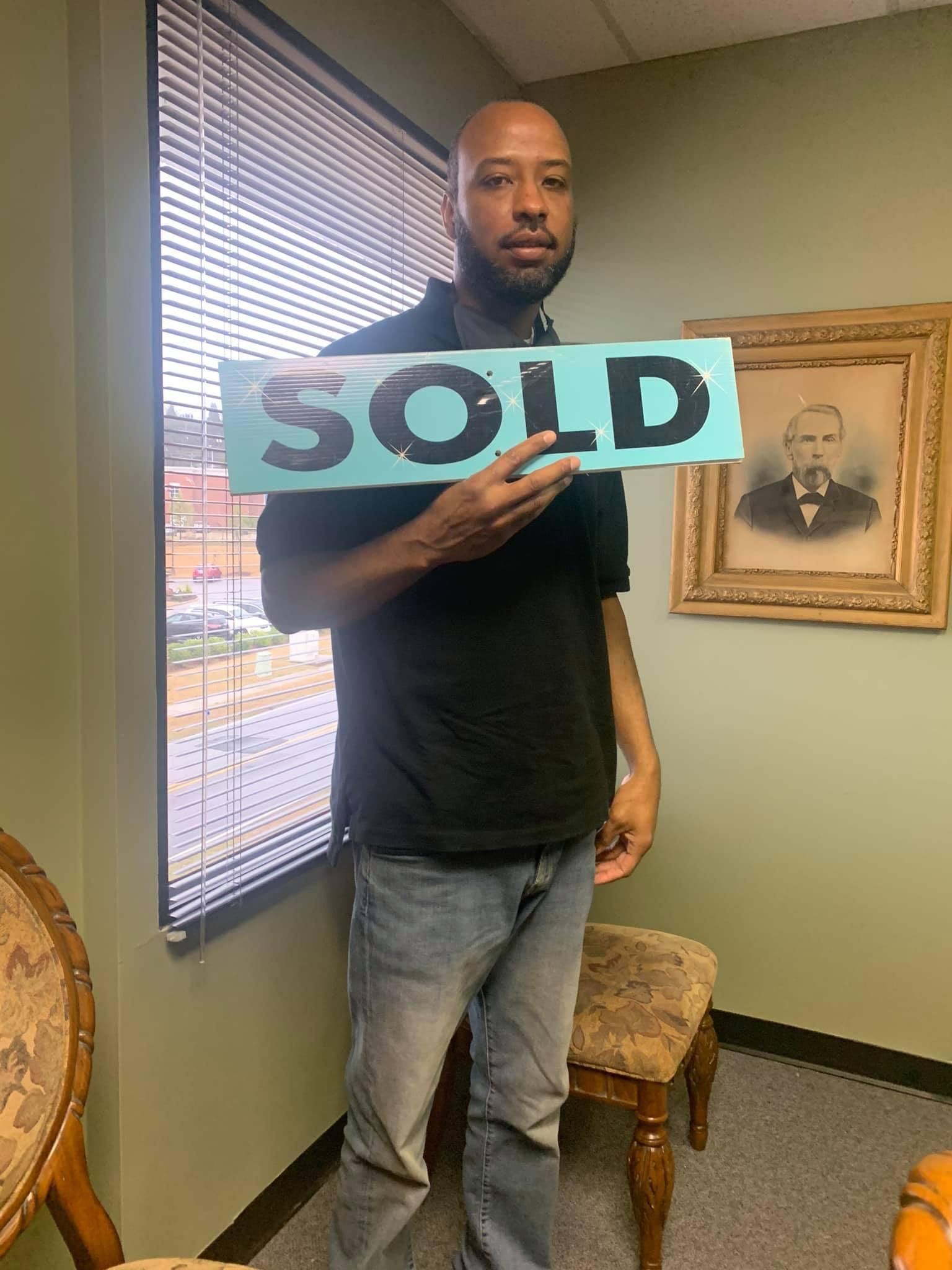 A man is holding a sold sign in front of a window.