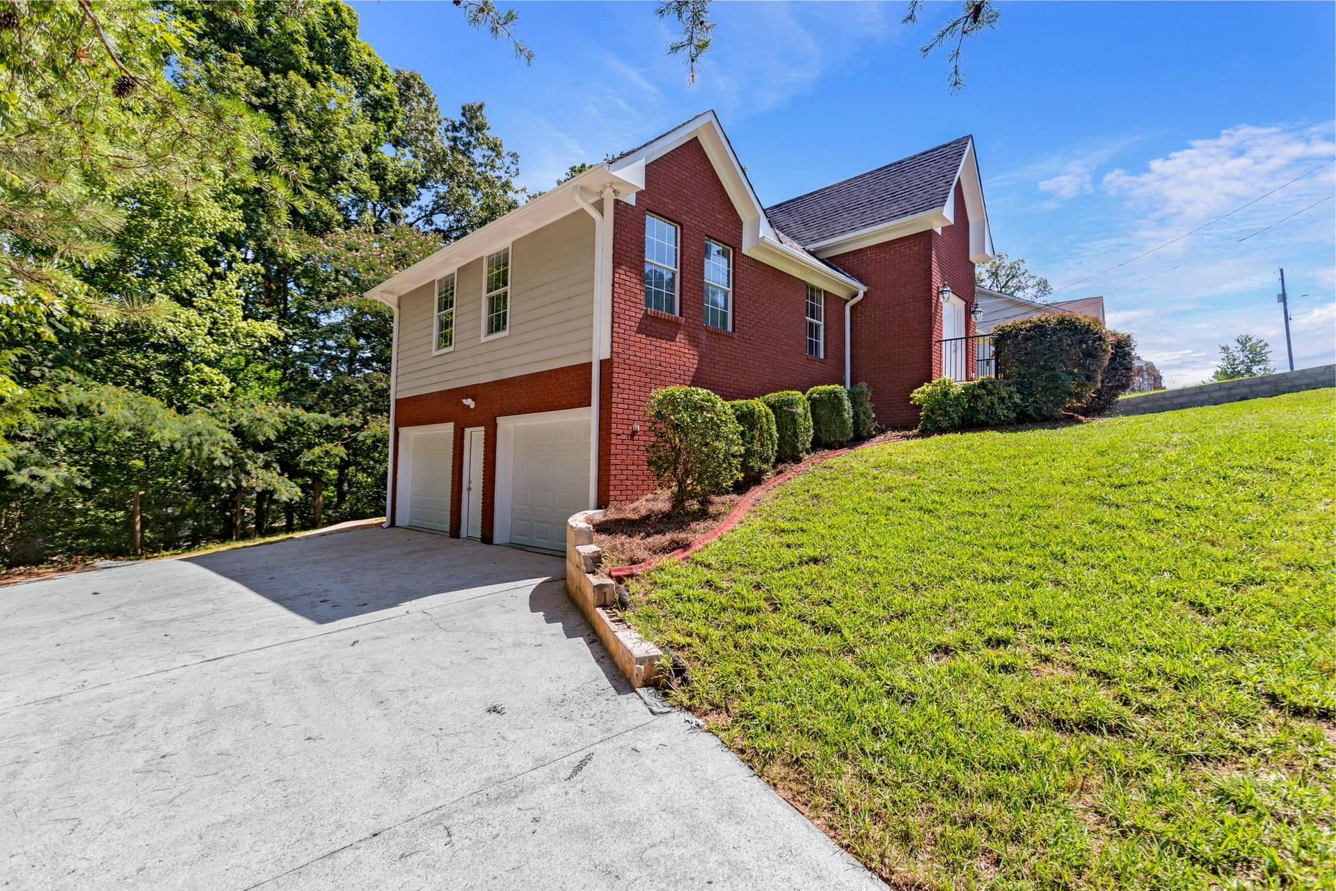 A red brick house with a garage is sitting on top of a lush green hillside.