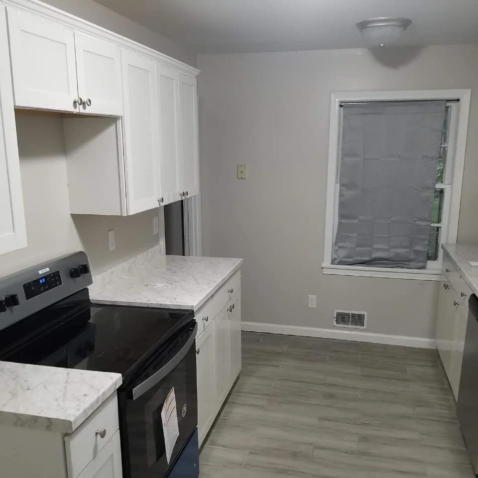 A kitchen with a black stove top oven , white cabinets , and a window.