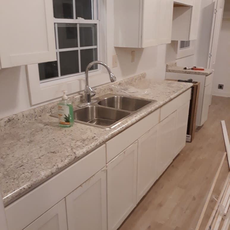 A kitchen with white cabinets , granite counter tops , a sink and a window.