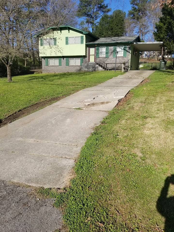 A green mobile home with a concrete driveway leading to it.