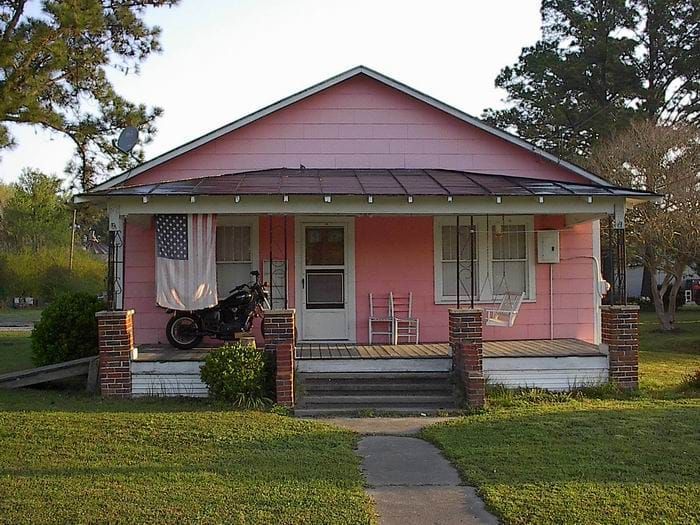 A pink house with a motorcycle parked on the porch