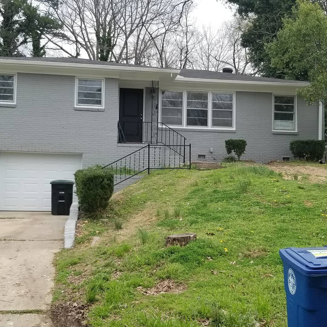 A gray house with a blue trash can in front of it.