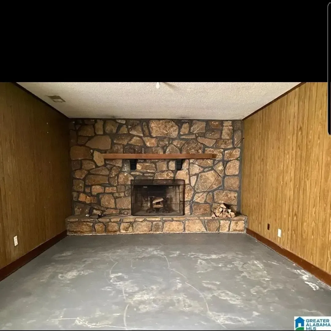 An empty living room with a stone fireplace and wood paneling.