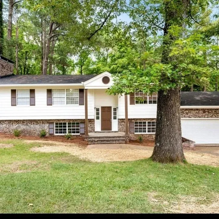A white house with a tree in front of it surrounded by trees.
