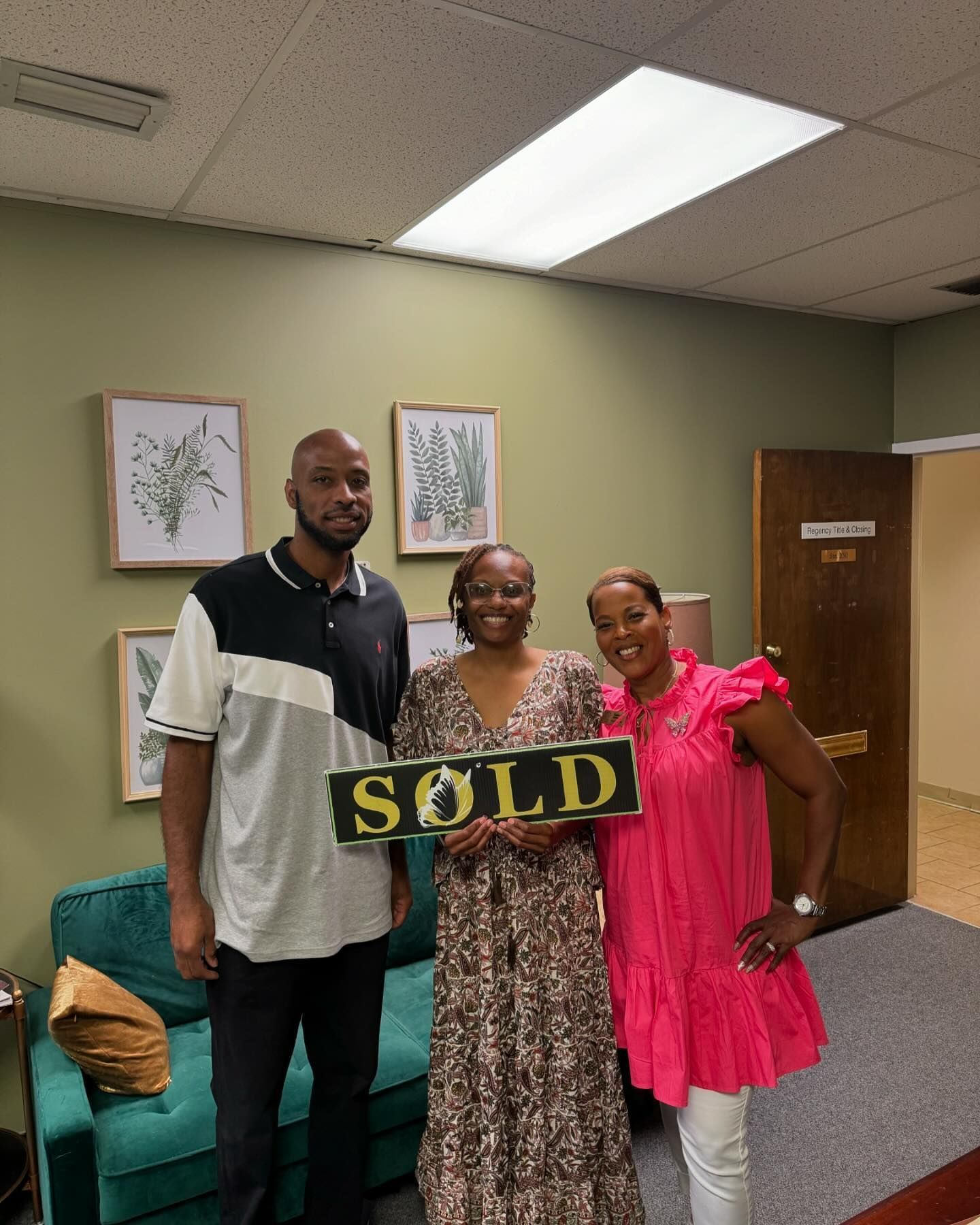 A man and two women are standing next to each other holding a sold sign.