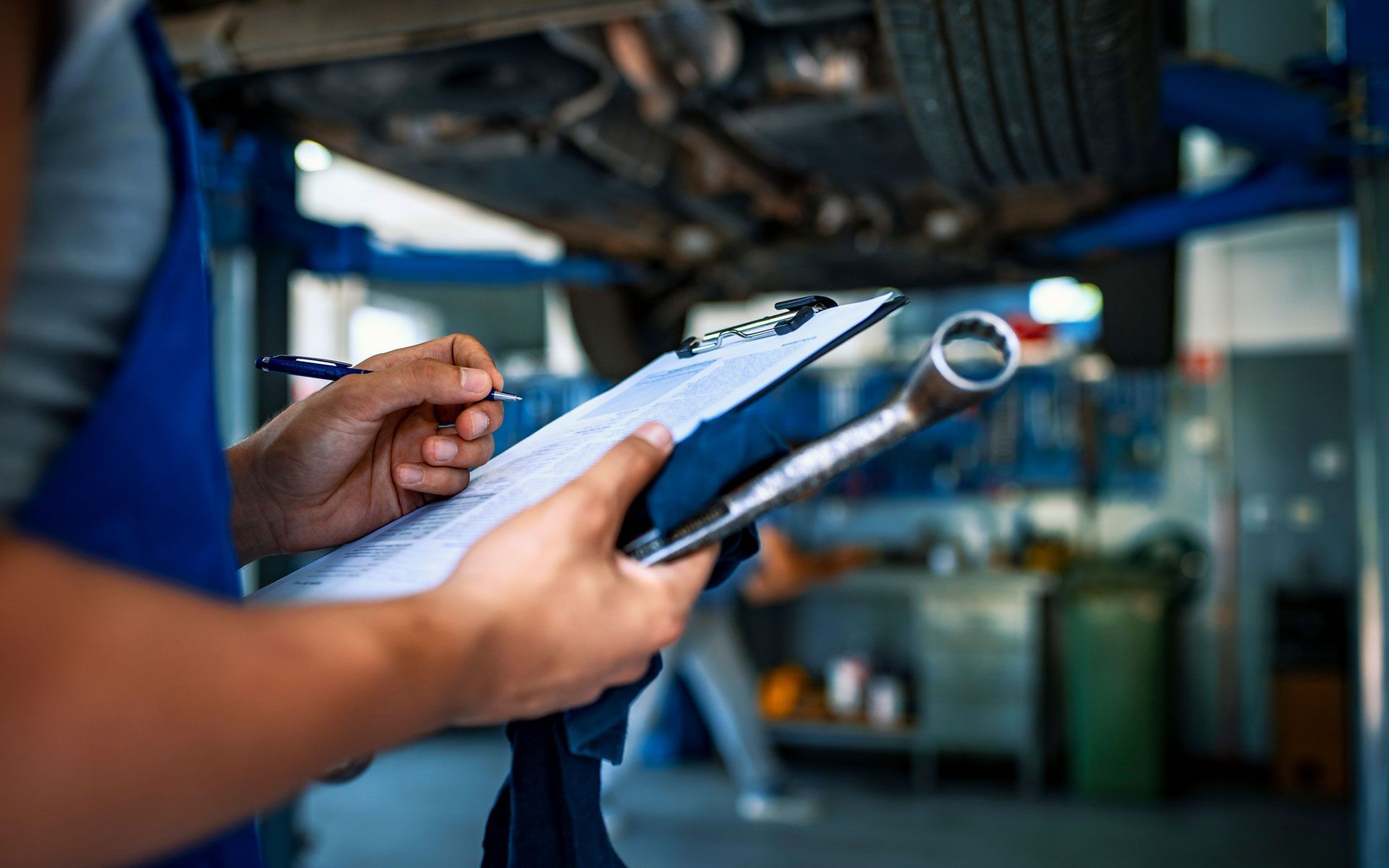 A mechanic is holding a clipboard and a wrench in a garage.