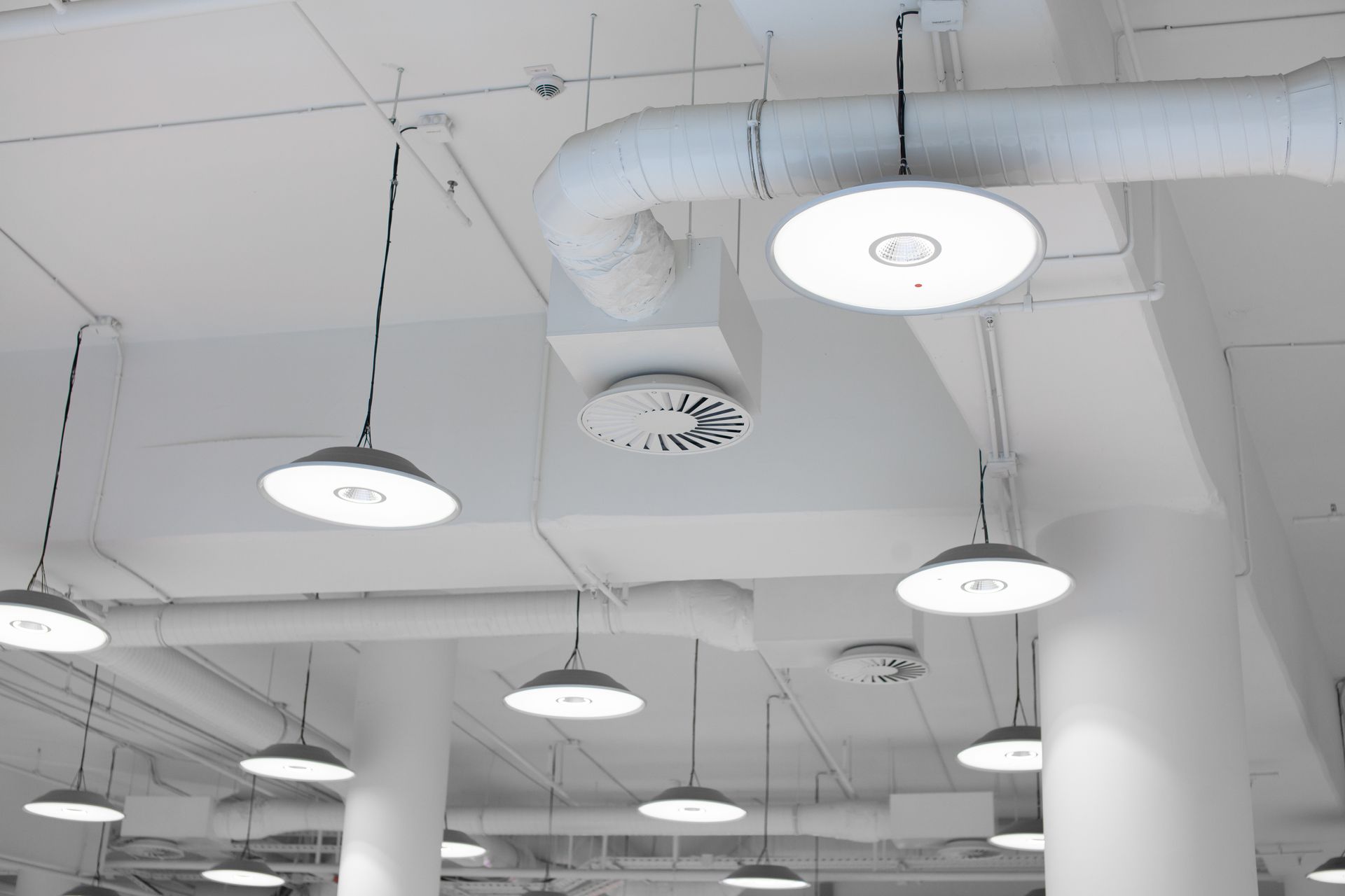 White ceiling with hanging lights, air ducts, and ventilation system.