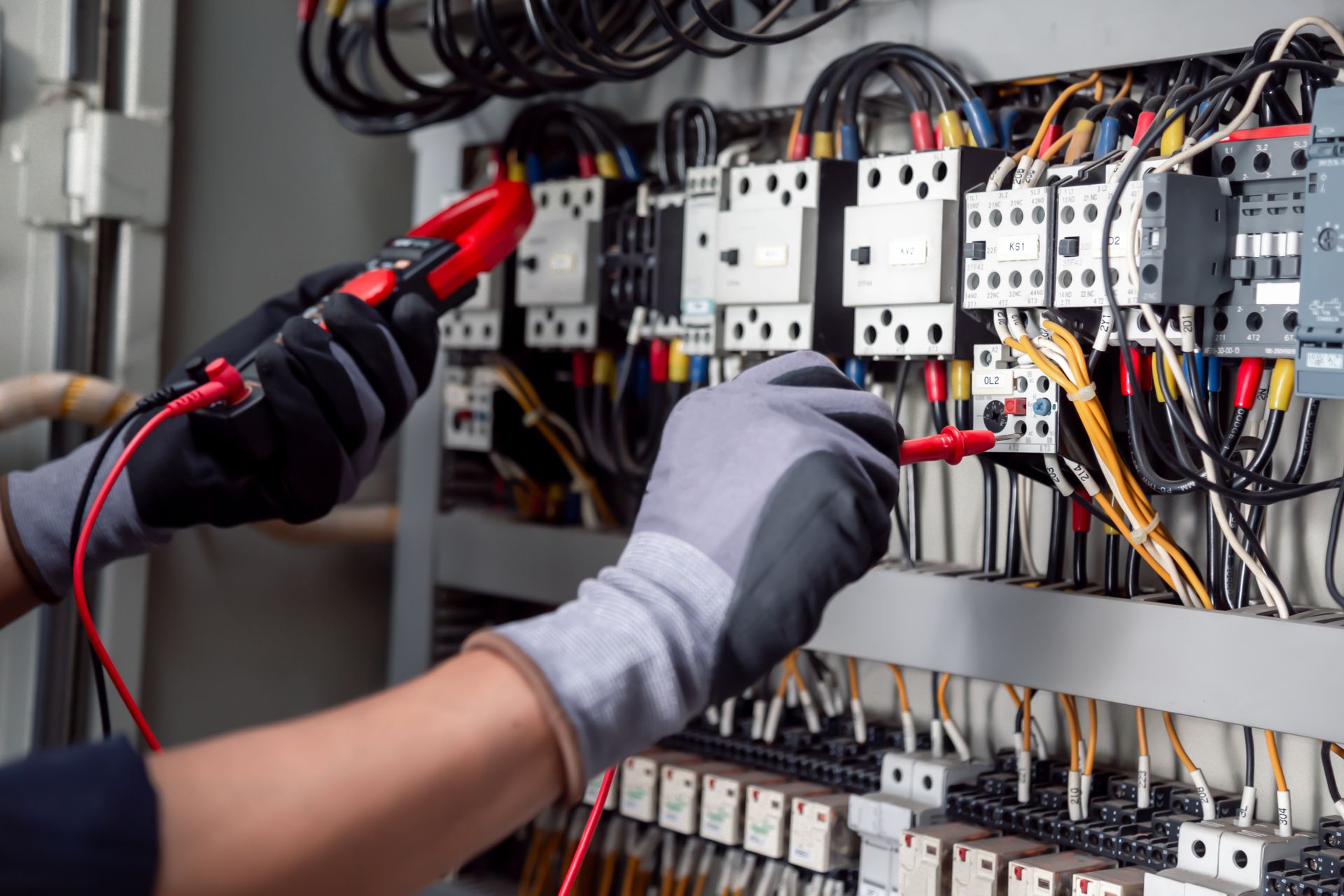 Electrician testing wires in electrical panel with a multimeter, wearing gloves.
