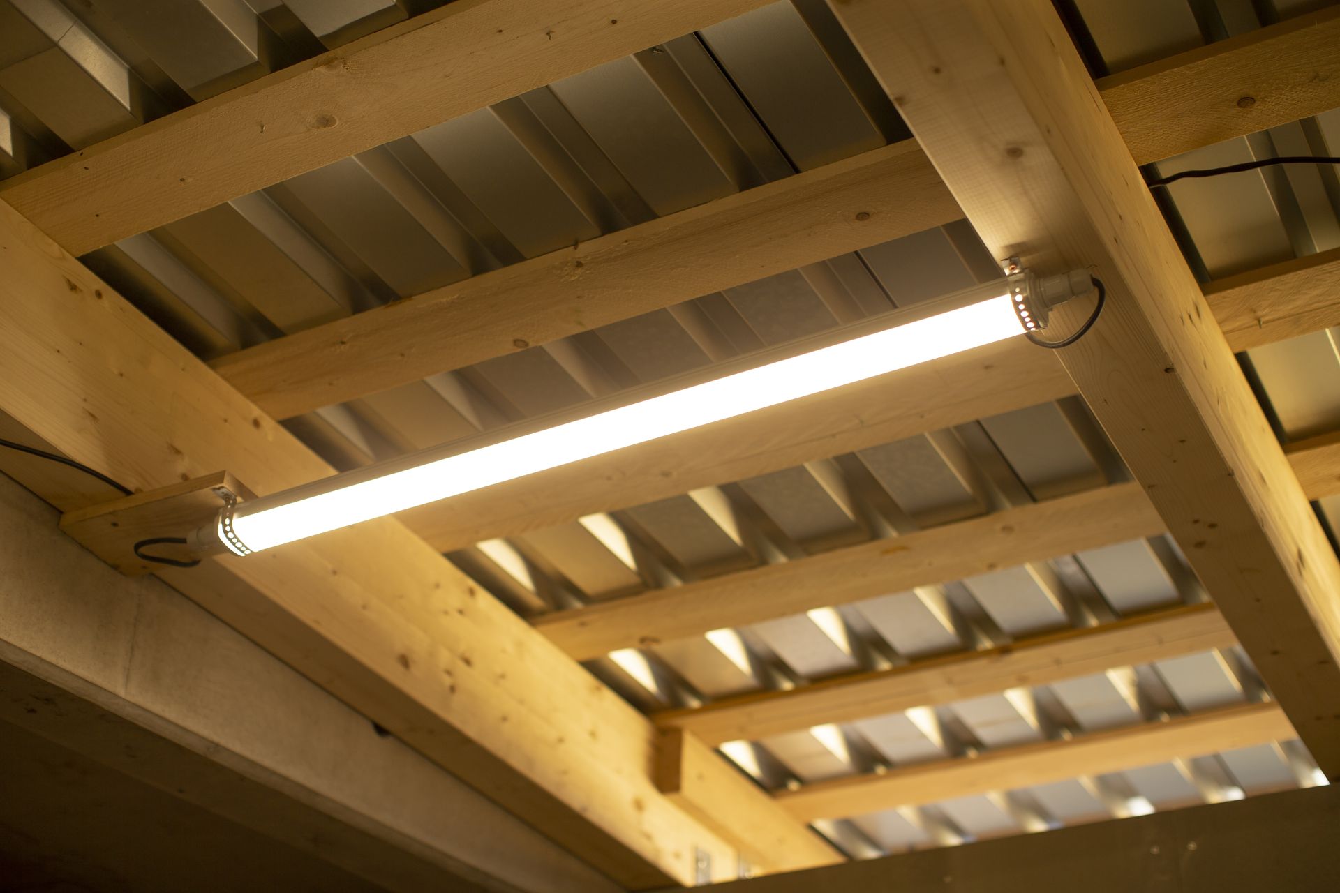 Fluorescent light fixture attached to wooden beams and a corrugated metal ceiling.