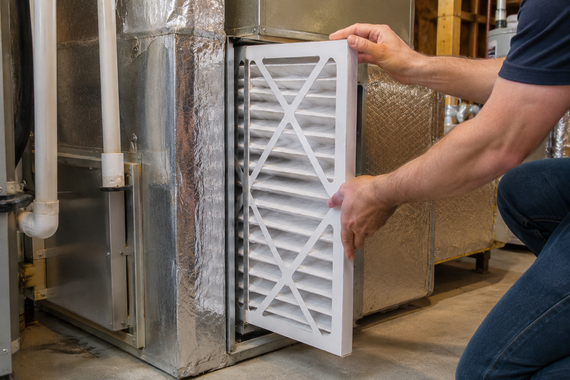 Person installing a white furnace air filter in a metal HVAC unit in a utility room