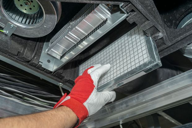 Gloved hand holding a rectangular filter inside a car’s air vent system