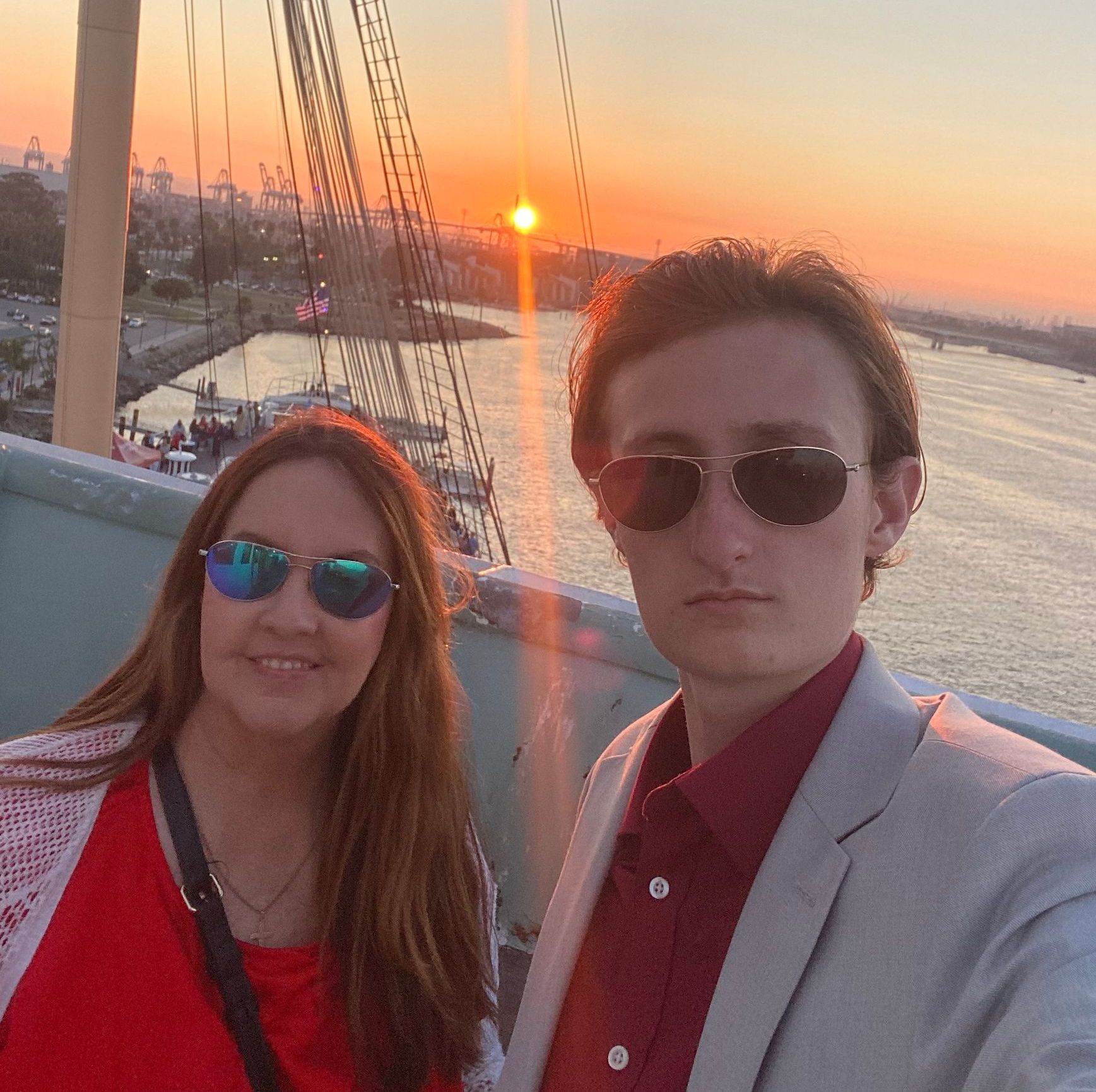 A man and a woman are standing next to each other in front of a body of water at sunset.
