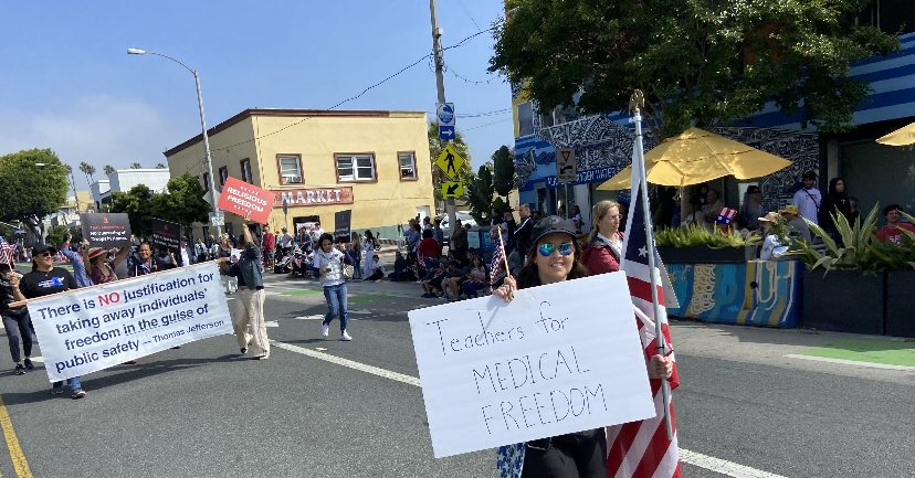 A street demonstration. People carry signs for medical freedom and the right to bodily autonomy, marching on a sunny day.