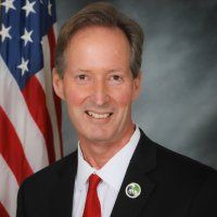 John Cruikshank, former Mayor of Rancho Palos Verdes A man in a suit and tie is standing in front of an american flag.