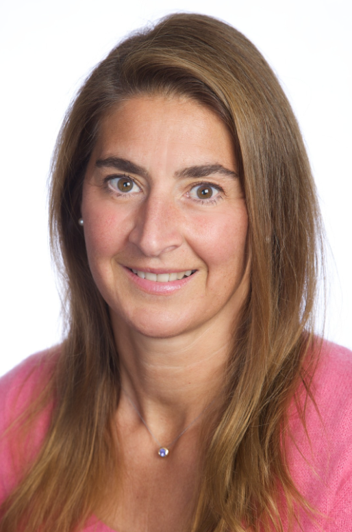 Leslie Manookian Woman with long brown hair, smiling, wearing a pink sweater. She has a small necklace and is set against a white background.